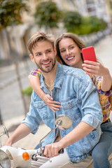 Woman taking picture with her boyfriend ridig a scooter