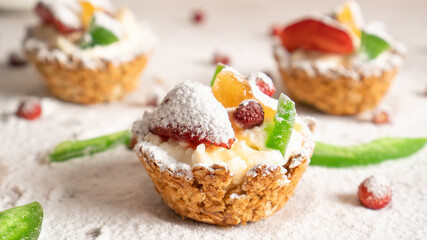 Obraz na płótnie Canvas Oat cupcakes with cottage cheese filling. Red strawberry, yellow and green dried fruits and icing sugar sprinkled around