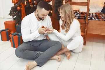 Obraz premium Couple near christmas tree. Lady in a white pajamas. Man in a white shirt.