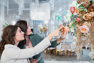 Beautiful women, girls florists in stylish suits in restaurant looking at floral composition....