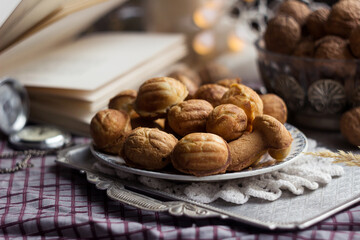 Cookies in the form of walnuts on a metal tray on a checkered tablecloth, next to them are real nuts in a shell in a vase, an open book, a clock