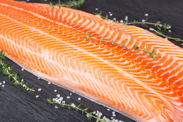 Half raw salmon fillet, salt and thyme on black wooden table