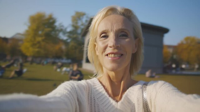 Pov shot of happy beautiful retired woman whirling and smiling in city park
