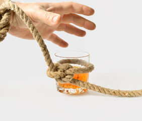 a glass with alcohol is tied in a knot of a rope, a man's hand is trying to take a glass, the concept of treatment for alcoholism, drunkenness in the family.