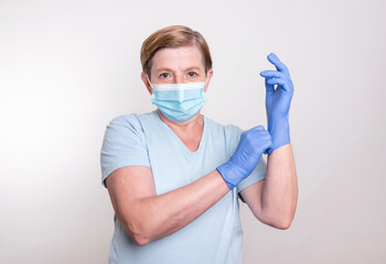 Elderly woman wearing gloves and putting on mask to stay safe and prevent spreading corona virus