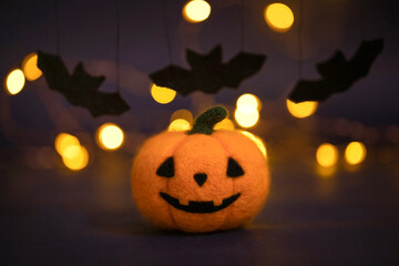 Halloween pumpkin and bats on a dark background with bokeh lights. The pumpkin toy is made of wool....