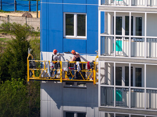 construction workers installers high-rise workers industrial climbers, painters on the lift paint...