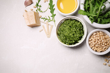Bowl of tasty arugula pesto and ingredients on light table, flat lay. Space for text