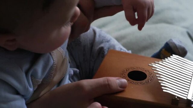 Parent spending time with family during coronavirus lockdown - father teaches little cute baby boy how to play tiny instrument calimba at home. Selective focus on instrument.