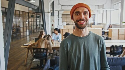 Portrait of positive man manager smiling to camera at office with colleagues, tracking shot