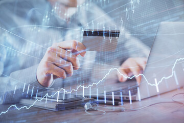 Double exposure of man hands holding a credit card and Forex graph drawing. Stock trading and digital fintech in Internet E-commerce concept.