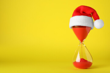 Hourglass and Santa hat on yellow background, space for text. Christmas countdown