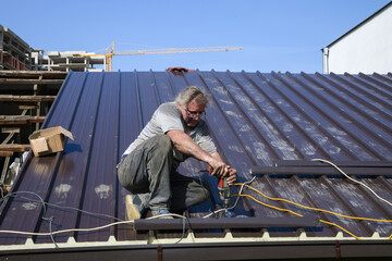 Repairing the roof of the house with screws drive tools. Worker roofer builder working on roof...