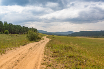 Summer mountain landscape. A rural road against the background of mountains in the Cis-Baikal basin. Irkutsk region, Russia