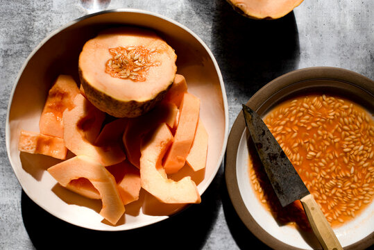 Canteloupe cut in half with slices in a bowl and seeds on a plate