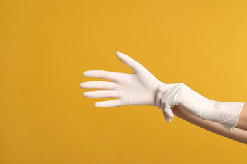 Doctor wearing medical gloves on yellow background, closeup