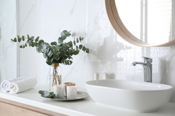 Fresh eucalyptus branches and burning candles on countertop in bathroom - obrazy, fototapety, plakaty