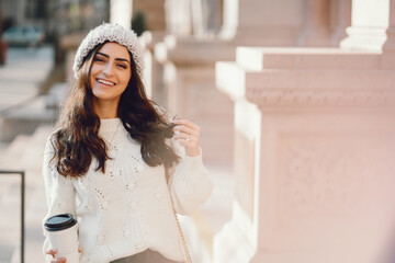 Fototapeta na wymiar Elegant girl standing in a winter city. Woman in a white knited sweater. Beautiful lady with dark hair.
