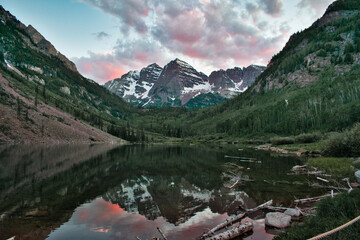 Maroon Bells in Aspen Colorado at Sunset. Beautiful maroon colors and pink clouds reflecting off glassy water. Reflection of mountain tops on water framed between cliffs and trees