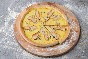 Whole meat Pizza with chicken fillet slices, champignon mushrooms, cream sauce and a lot of mozzarella cheese served on wooden plate served with culinary flour and spices on gray concrete background.
