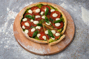 Whole Italian Caprese Pizza with sliced tomatoes, mozzarella cheese, pesto sauce served with fresh...