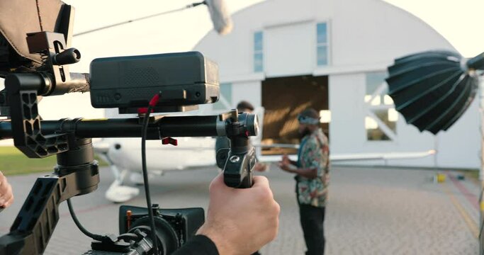 Camera approaching multi-ethnic male actors standing outdoors on set. Professional cameraman filming scene. Caucasian man giving money to African American guy and hugging him. Close up concept