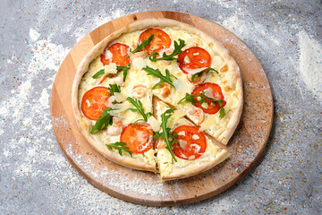Whole seafood Pizza with cocktail prawns, tomato slices, cream sauce  served with fresh arugula Leaves on wooden plate served with culinary flour and spices on gray concrete background.
