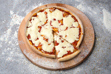 Whole classic Italian Margarita Pizza with tomatoes and mozzarella cheese served on wooden plate served with culinary flour and spices on gray concrete background.
