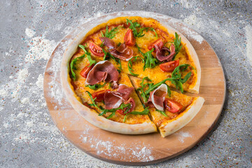 Whole Italian Pizza on wooden plate served with flour and spices on gray concrete background. Dish...