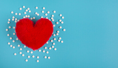 Concept heart disease. Red heart and white tablets on a blue background with space for text