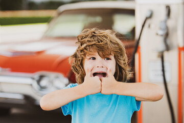 Child boy with retro car at the vintage petrol station thumbs up.