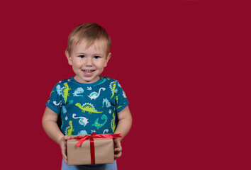 A little boy tries to unpack a New Year's gift smiling on a red background