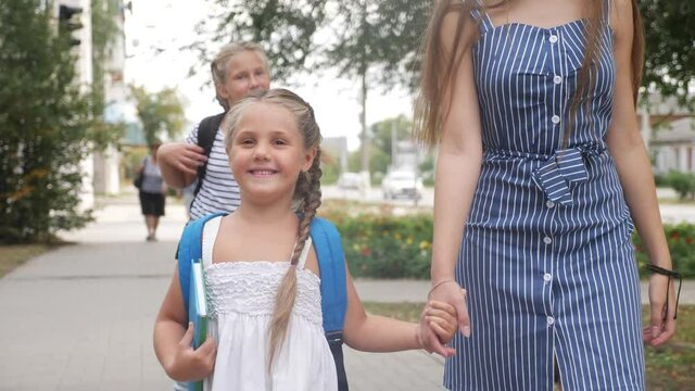 mom and daughter go to school. happy family school education concept. schoolgirl with mom go hand in hand to school on footpath in the park. little girl with a briefcase time to lifestyle study