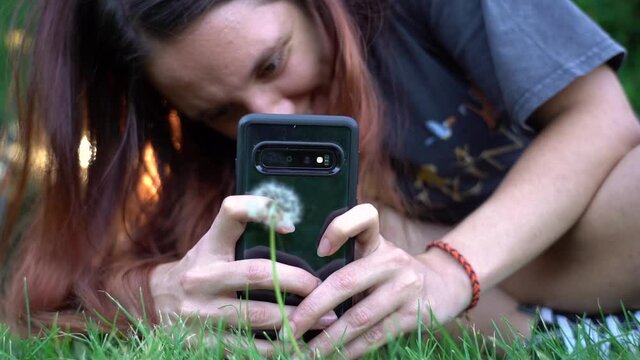 Young woman taking pictures with her Smart phone of a pretty dandelion
