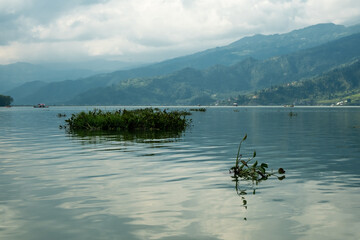 Waves on the surface of the lake water. Buildings on the shore. In the distance, the mountains are lost in the fog. Massive clouds above them