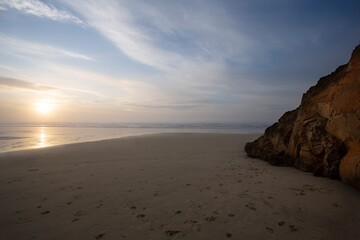  An eye level view of the ocean from the beach at sunset with blue sky and wispy clouds
