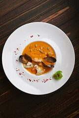 Creamy pumpkin soup with seafood, mussels, shrimps, squids, in a white plate, on a wooden background