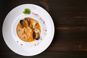 Creamy pumpkin soup with seafood, mussels, shrimps, squids, in a white plate, on a wooden background