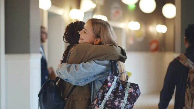 Two diverse female college classmates meeting and hugging in school corridor