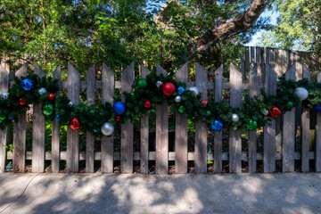 A light colored textured wooden paling fence with a Christmas garland looped along the middle of...