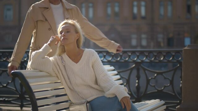 Senior man coming behind and closing eyes of woman sitting on bench by riverside