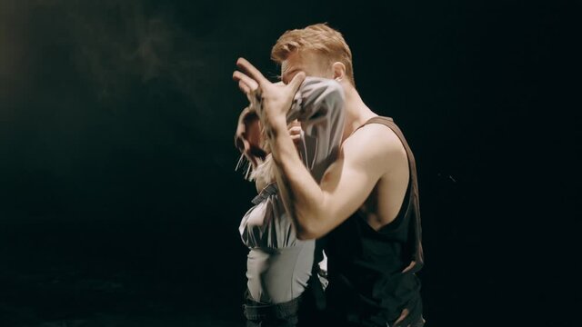 Young man and woman dancers performing in the dark lighted room. Couple dancing on stage with smoke background.