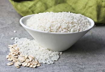A porcelain bowl with white rice and oatmeal is on the kitchen table, with a light green tablecloth in the background.