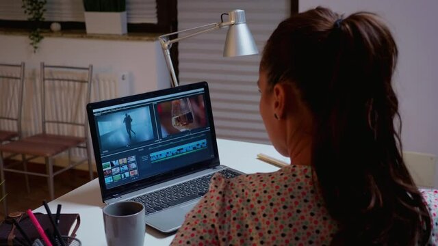 Movie maker editing a film using modern software for post production. Videographer working on audio film montage on professional laptop sitting on desk in modern kitchen in midnight
