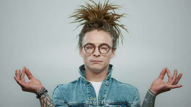 Stylish man meditating on grey background. Tattooed guy showing gyan mudra
