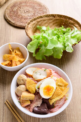 Thai food (Yen Ta Fo), Rice noodles soup with red sauce and fish tofu, pork ball and fried wonton in a bowl with chopsticks on wooden background