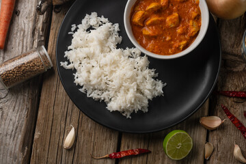 Top view of plate with classic chicken curry and rice served with lime, garlic and red hot chilli on rustic wooden table background. Traditional Indian cuisine. Spices for taste.