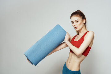 Woman holds in hand a mat for fitness sport slim figure exercises light background