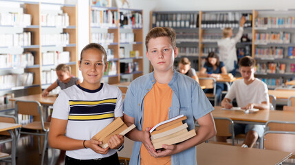 Portrait of teenage boy and girl holding books in school library