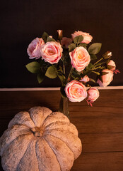 Brown pumpkin and roses on black background. Still life photograph with pumpkin and roses